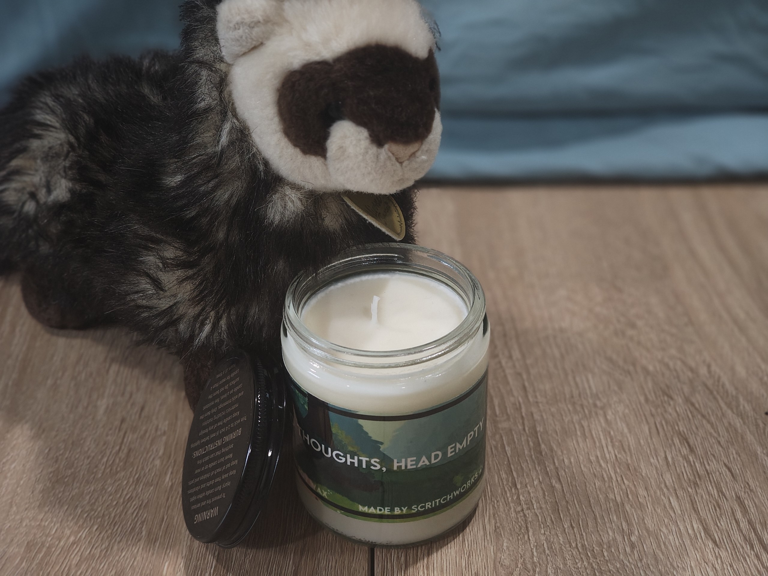 Scritch Plush sitting with a No Thoughts, Head Empty candle!