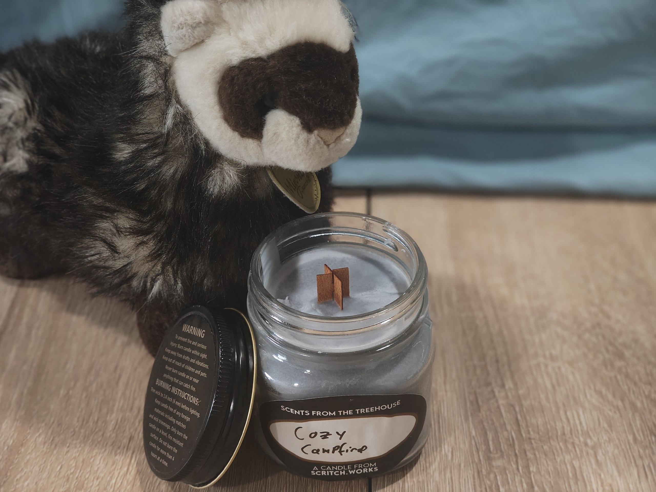 Scritch Plush sitting with a Cozy Campfire candle!